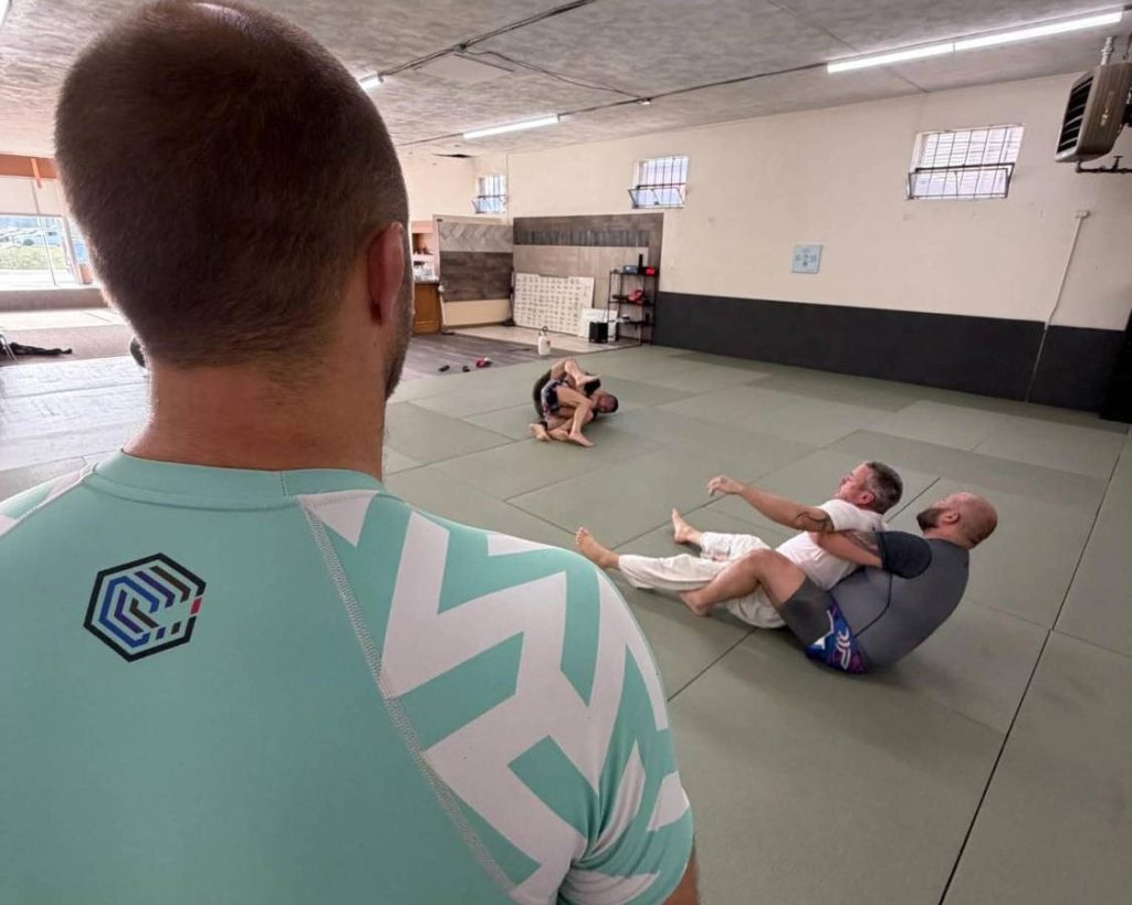Coach Jacob in a Consecution rash guard watching adult students roll