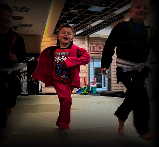A young student in a red gi laughing during kids Jiu-Jitsu class
